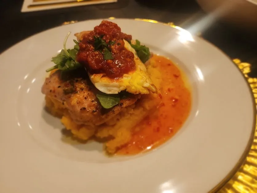 Fine-dining plate of seasoned chicken over creamy grits with red pepper relish